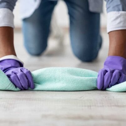 Unrecognizable black guy cleaning floor with dust cloth, wearing colorful rubber gloves, closeup. Cropped of african american man house-keeper erasing floor, cleaning house alone